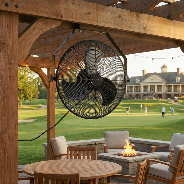 Outdoor patio with wooden pergola and MULE outdoor fan, table, chairs, and fire pit overlooking a golf course.