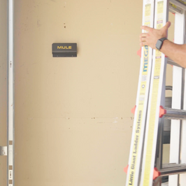 Person using a ladder with a MULE wall bracket on a wall.