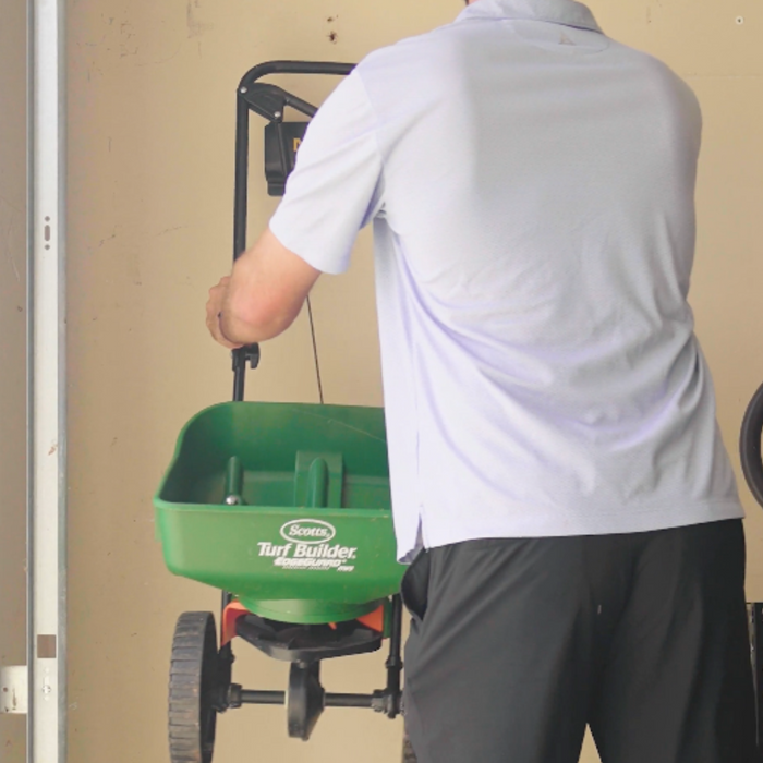 Person hanging a green fertilizer spreader labeled 'Turf Builder' on a Mule wall bracket tool organizer. 